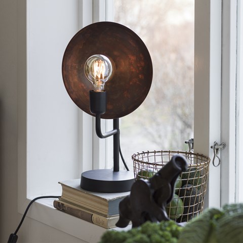 Metalowa lampa stołowa o surowym, rdzawym wykończeniu z widoczną żarówką dekoracyjną - kwintesencja stylu loftowego.
