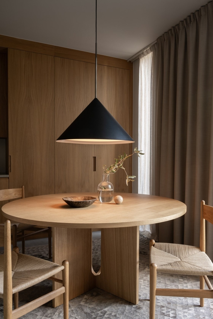 Minimalistyczna jadalnia z drewnianym stołem i czarną lampą stożkową.